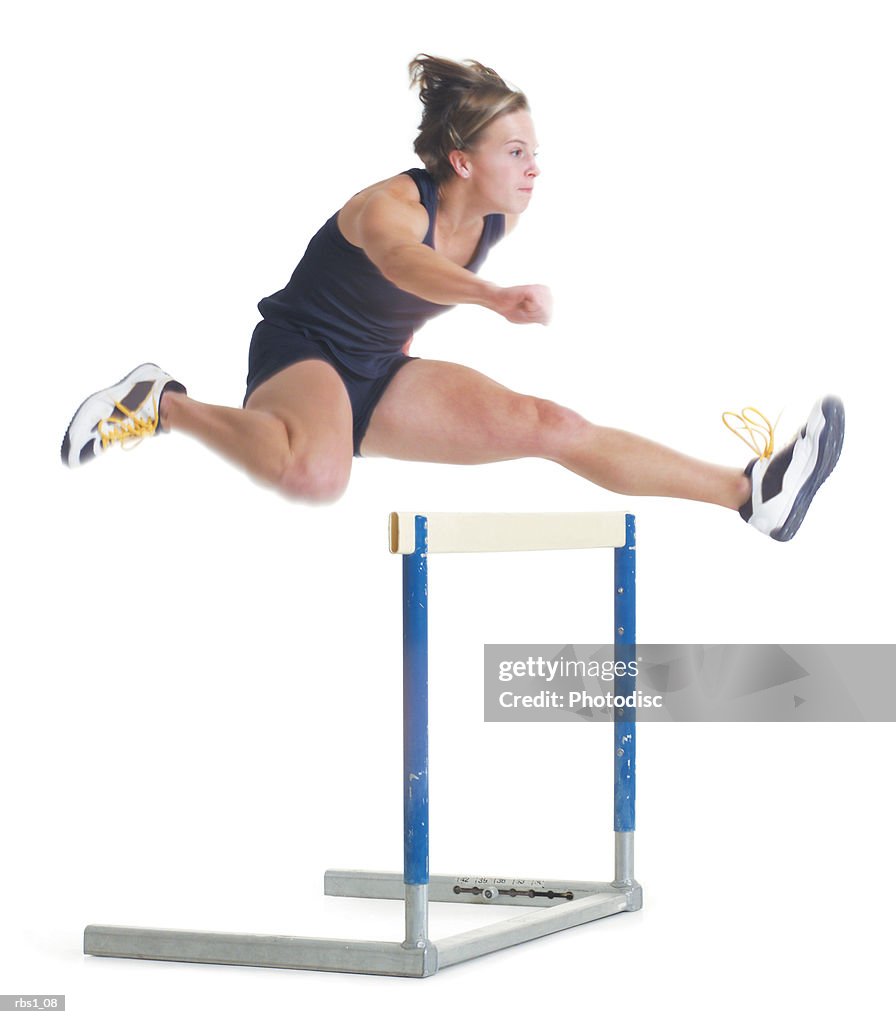 A young female caucasain runner wearing a black uniform is jumping over a hurdle