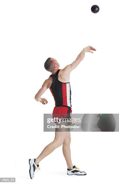 a young caucasian man wearing a red track uniform is turning around as he throws a shotput - men's field event stockfoto's en -beelden