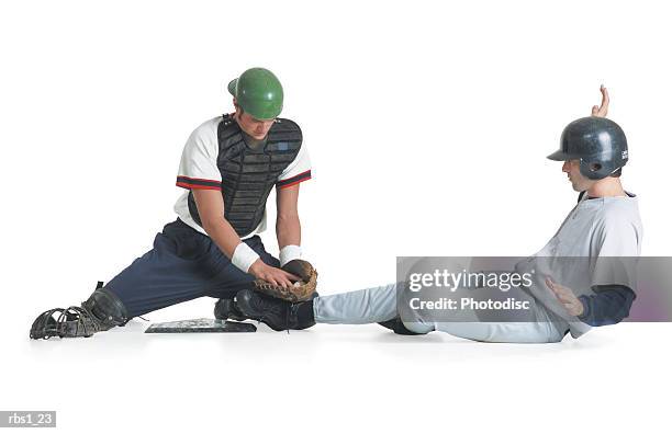 two caucasian men are dressed in baseball uniforms as one in a catcher vest tags the other wearing a batter helmet out - vangershandschoen stockfoto's en -beelden