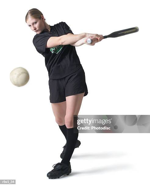 a pretty young caucasian woman is wearing a black softball uniform and swinging her bat after hitting a ball - baseball bat and ball stock pictures, royalty-free photos & images