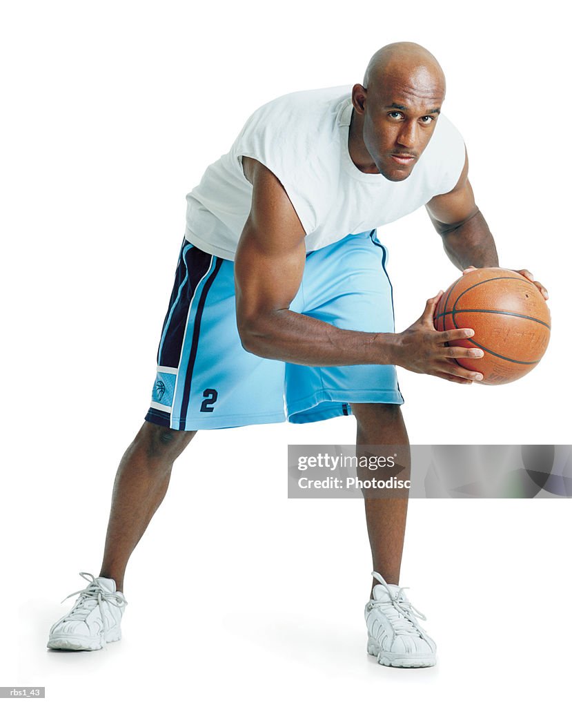 A bald african american man dressed in powder blue basketball shorts and is leaning forward holding a ball preparing to pass