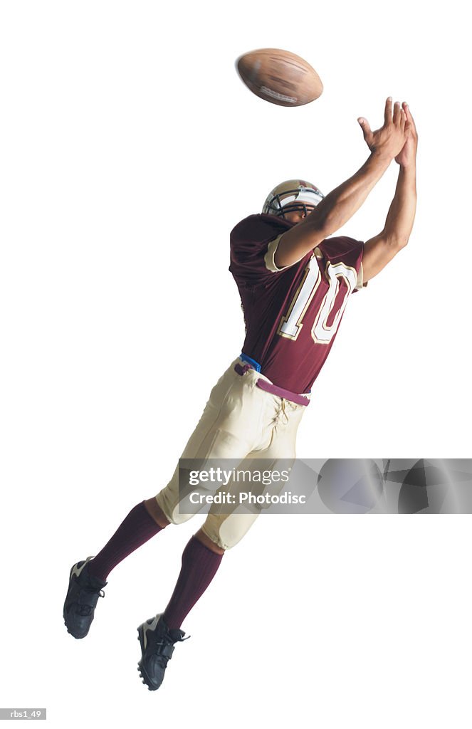 An african american football player in a red and white uniform is jumping up with arms outstretched to catch a football
