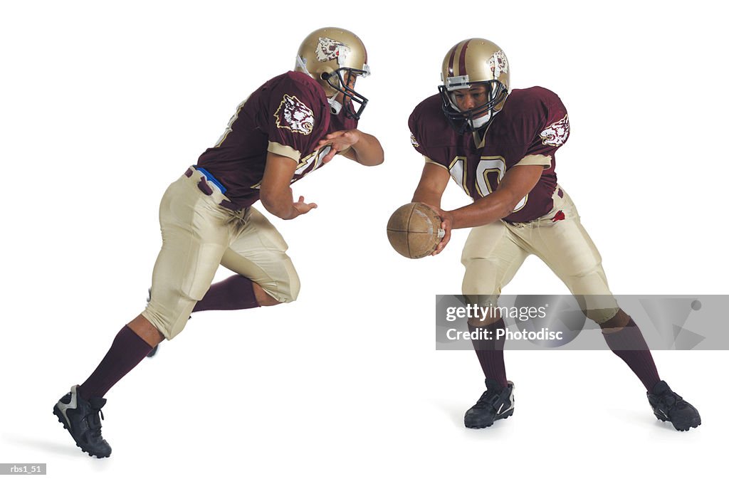 Two african american football players wearing red and white uniforms are running towards each other as one prepares to pass the ball to the other