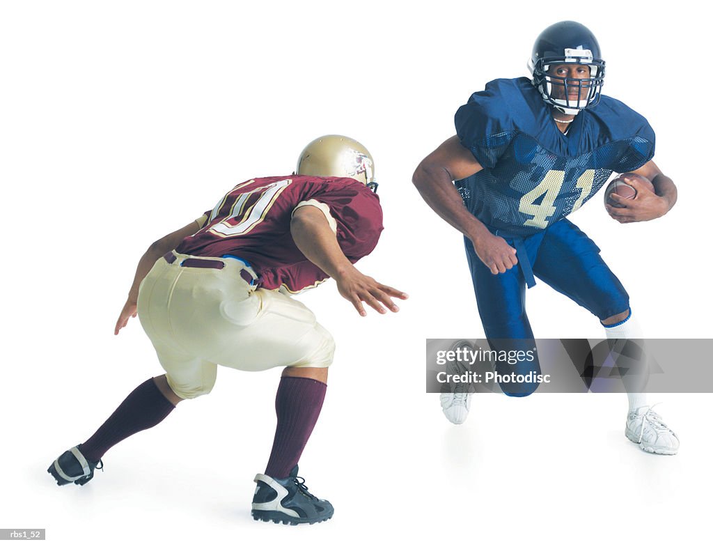 Two football players from opposing teams are running towards each other as one holds the football and the other crouches forward to stop him