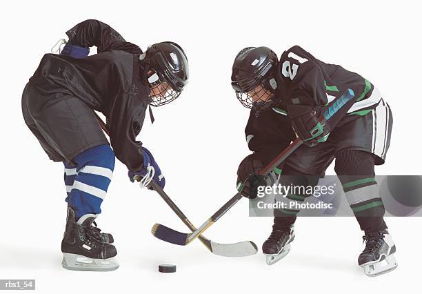 two caucasian hockey players wearing opposing uniforms are holding thier sticks and leaning forward trying to hit the puck - ijshockeytenue stockfoto's en -beelden