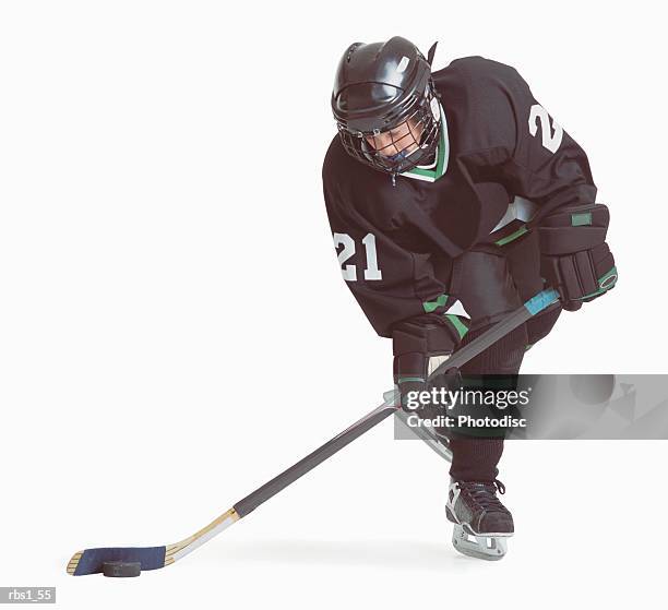 a caucasian hockey player wearing a black uniform is skating with his stick about to hit the puck - hockey puck white background stock pictures, royalty-free photos & images