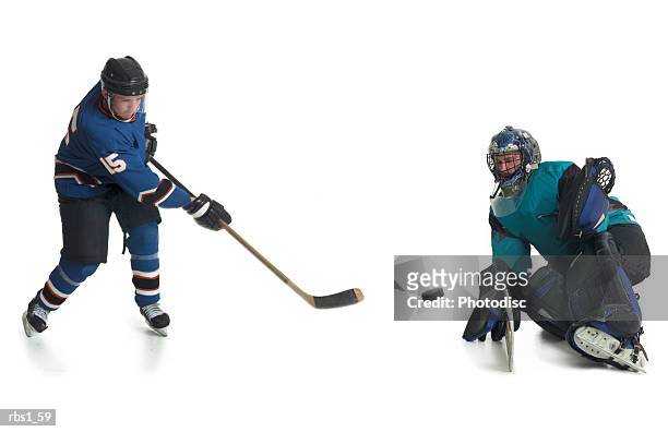 a caucasian male hockey player in a blue jersey skates and shoots his puck towards the goalkeepeer of the opposing team - ijshockeytenue stockfoto's en -beelden