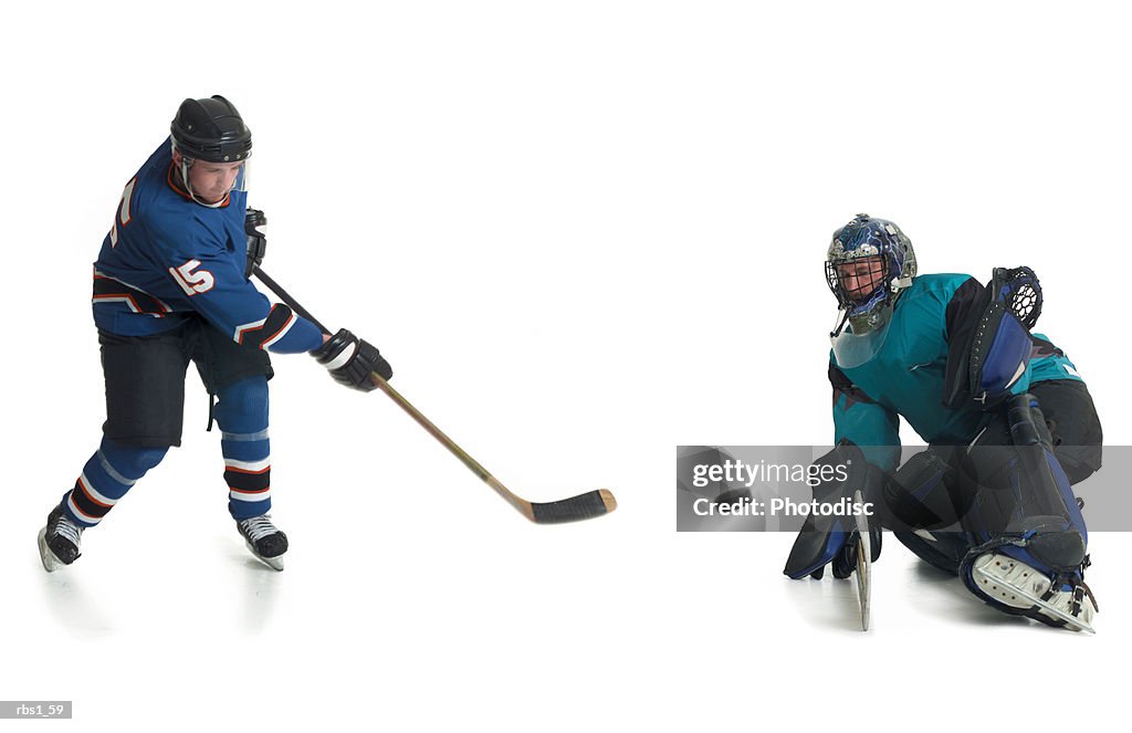 A caucasian male hockey player in a blue jersey skates and shoots his puck towards the goalkeepeer of the opposing team