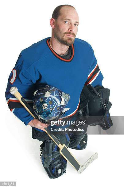 an adult bearded caucasian male hockey player holds his equipment and smiles smugly as he looks up at the camera - ijshockeytenue stockfoto's en -beelden