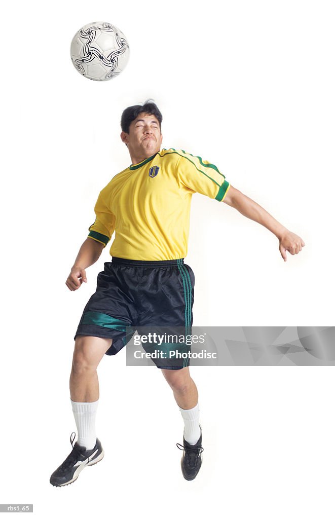 A young latin male wearing a yellow jersey jumps and hits a soccer ball with his head
