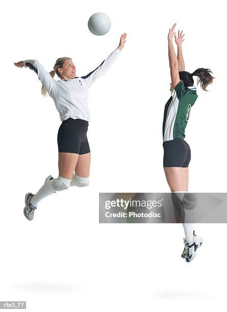 two young caucasian female volleyball players from opposing teams square off as one jumps and hits the ball while the other prepares to block - volleyball player photos et images de collection