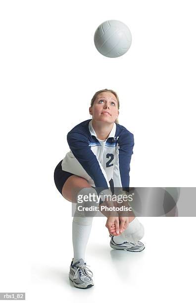 a young attractive caucasian female volleyball player in a blue and white jersey kneels forward preparing to hit a ball flying towards her - sporttrikot freisteller stock-fotos und bilder