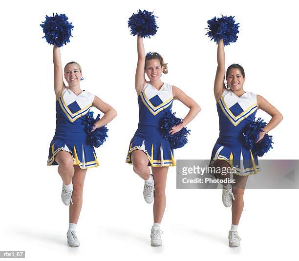 three teenage caucasian female cheerleaders in blue uniforms do a routine and raise their pom poms in the air - cheerleading stock-fotos und bilder