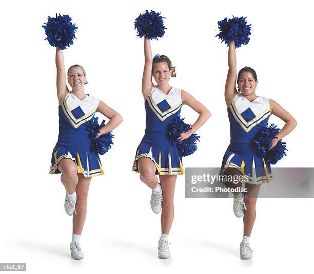 three teenage caucasian female cheerleaders in blue uniforms do a routine and raise their pom poms in the air - チアリーダー ストックフォトと画像