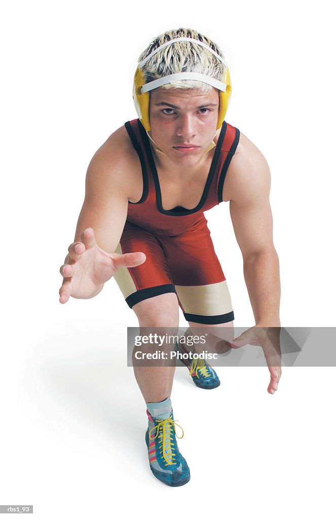 A teenage caucasian male wrestler in a red uniform stands ready to pounce