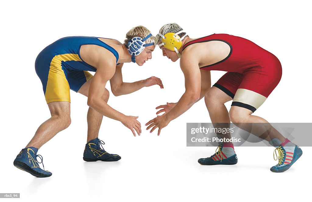 Two teenage caucasian male wrestlers from opposing teams face off at the beginning of a match
