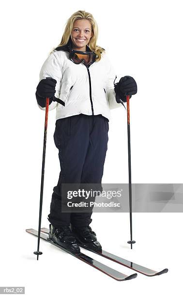 a young caucasian female skier in a white coat stands smiling with her snow skis and poles - snow white - fotografias e filmes do acervo