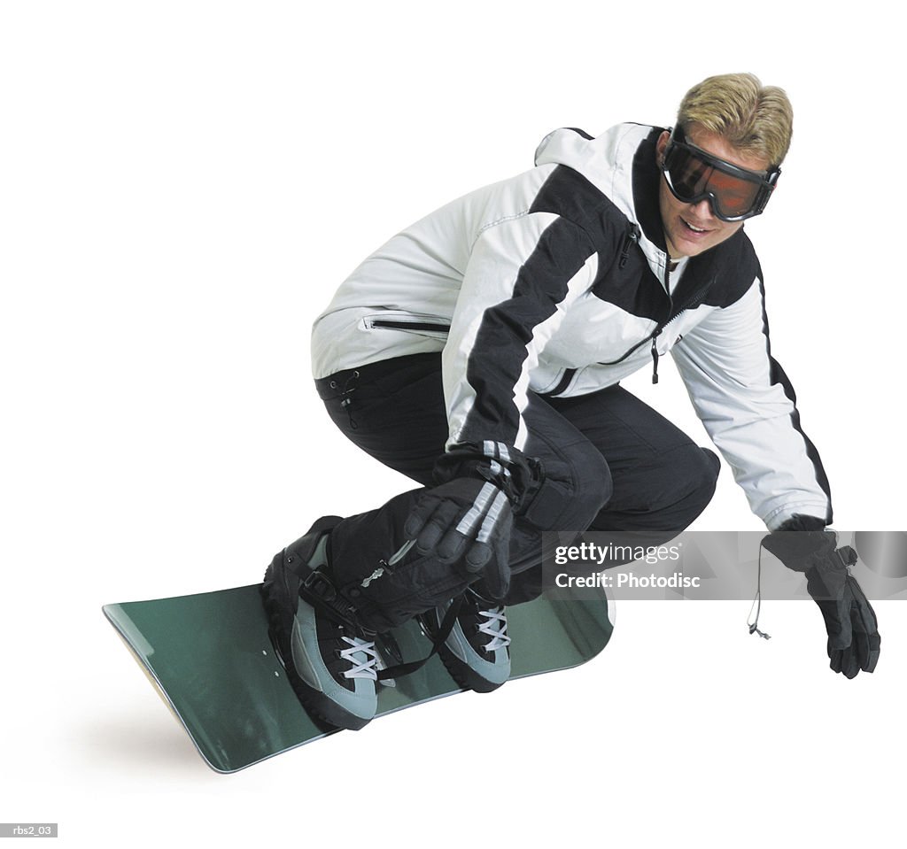 A young caucasian male snowboarder in a white and black jacket turns quickly while riding his board