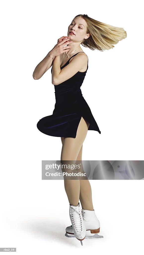 A young blonde caucasian female ice skater in a dark blue outfit spins and skates on the ice