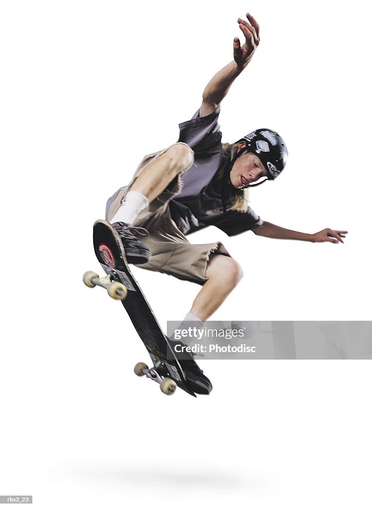 A teenage caucasian male jumps up in the air on his skateboard while raising his hands up in the air