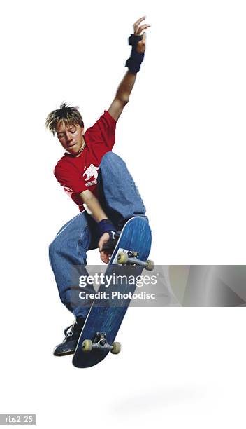 a teenage caucasian male skateboarder in a red shirt and blue jeans jumps his board while raising his arm up high - high up ストックフォトと画像