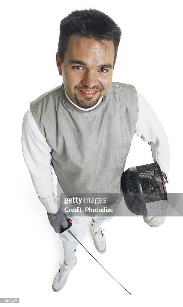 A caucasian male fencer holds his face mask and sword while he smiles and looks up at the camera