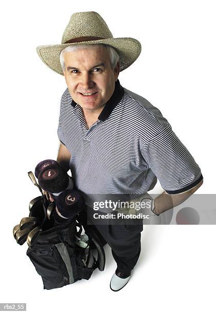 a middle age caucasian man is wearing a straw hat and a stripped golf shirt as he holds his gold bag and looks up at the camera - camera bag stock pictures, royalty-free photos & images