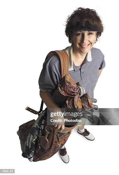 a middle age adult caucasian female golfer stands with her bag of golf clubs smiling and looking up at the camera - camera bag stock-fotos und bilder
