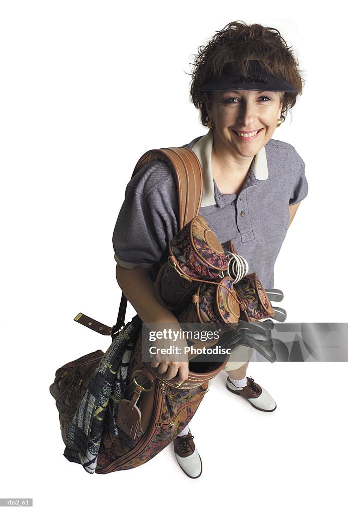 A middle age adult caucasian female golfer stands with her bag of golf clubs smiling and looking up at the camera