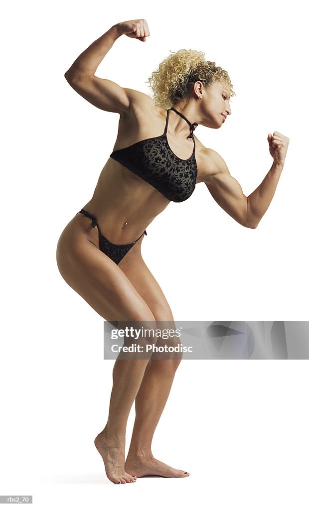 An adult caucasian female bodybuilder wearing a black bikini stands while flexing and posing for competition