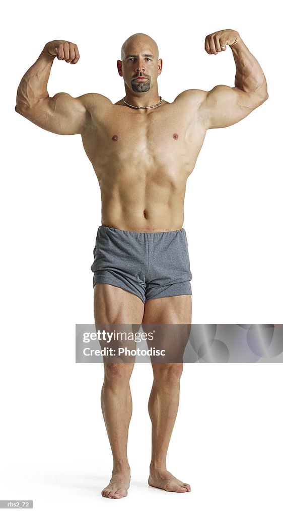 An adult caucasian male bodybuilder holds his arms up and flexes  his biceps and chest for competition