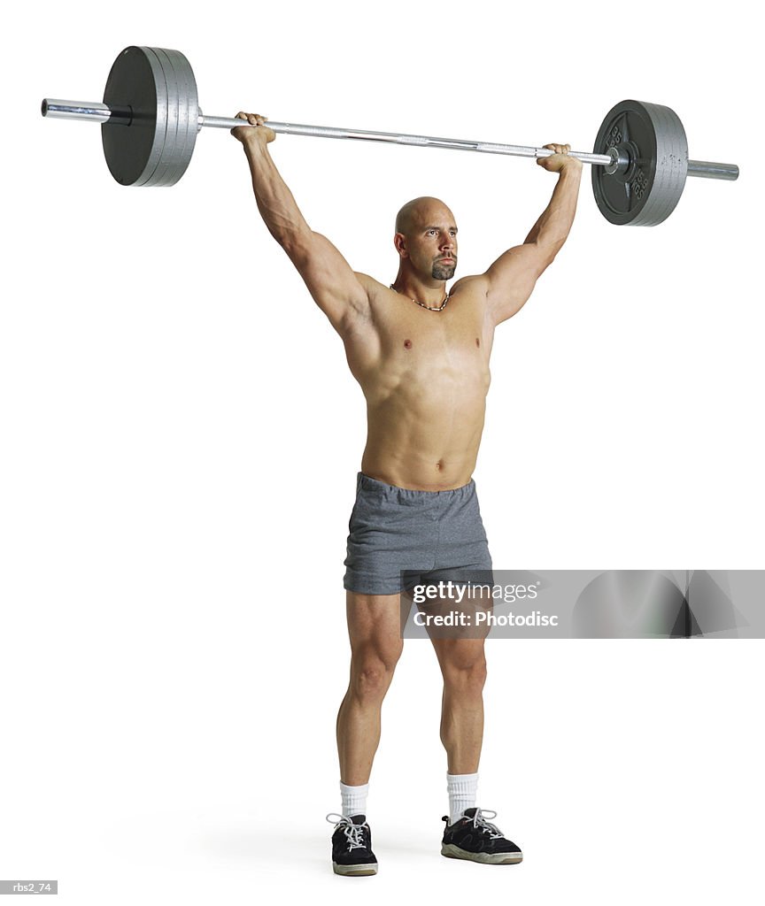 An adult caucasian male weightlifter in gray shorts stands with an extremely heavy weight raised high above his head