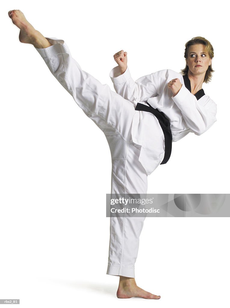 Adult caucasian female martial arts expert in white with blackbelt performs roundhouse kick to right