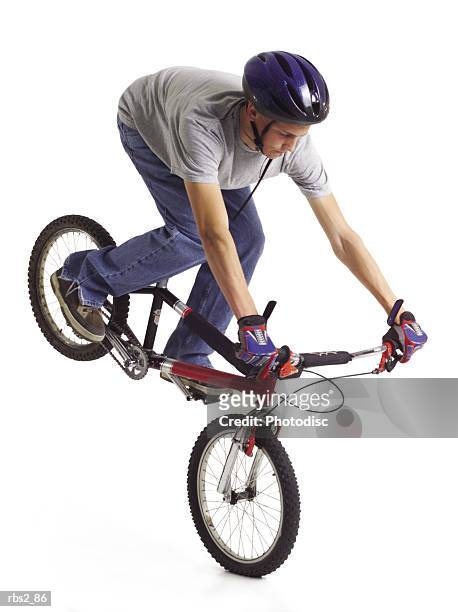 caucasian teenage boy wears blue bike helmet doing a stunt on red bike with rear tire in the air - bmx stock-fotos und bilder