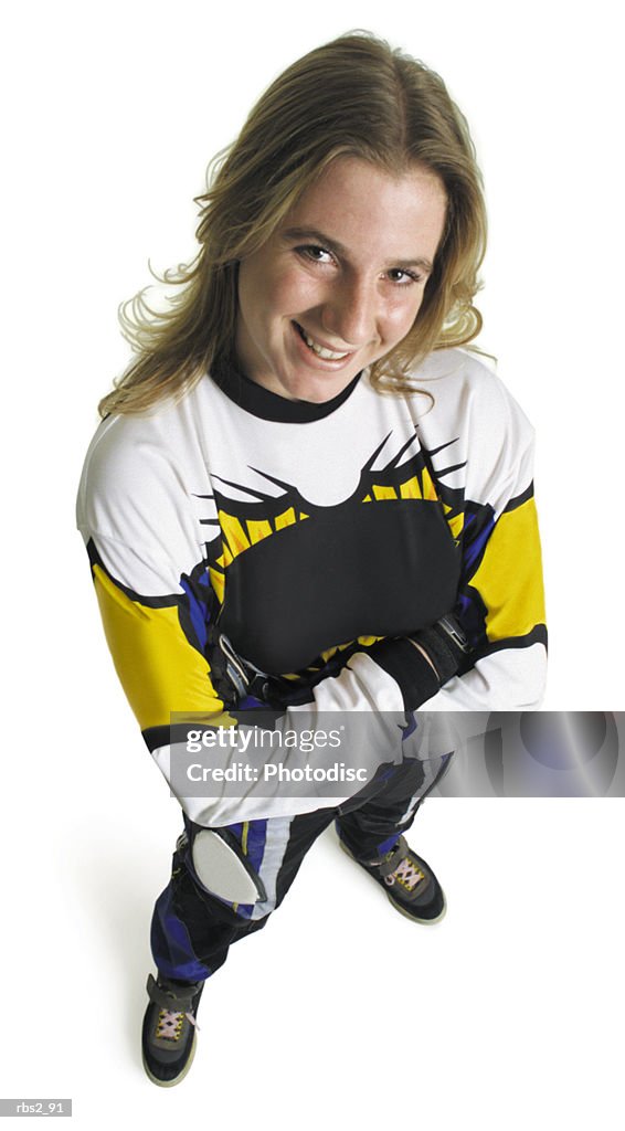 A blond caucasian teenage girl wearing a dirtbike racing suit is standing with arms crossed looking up at the camera