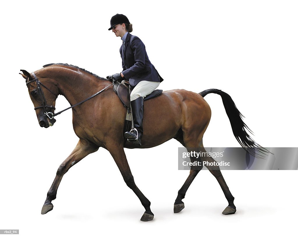 A young caucasian woman dressed in english equestrian clothes is riding a brown horse