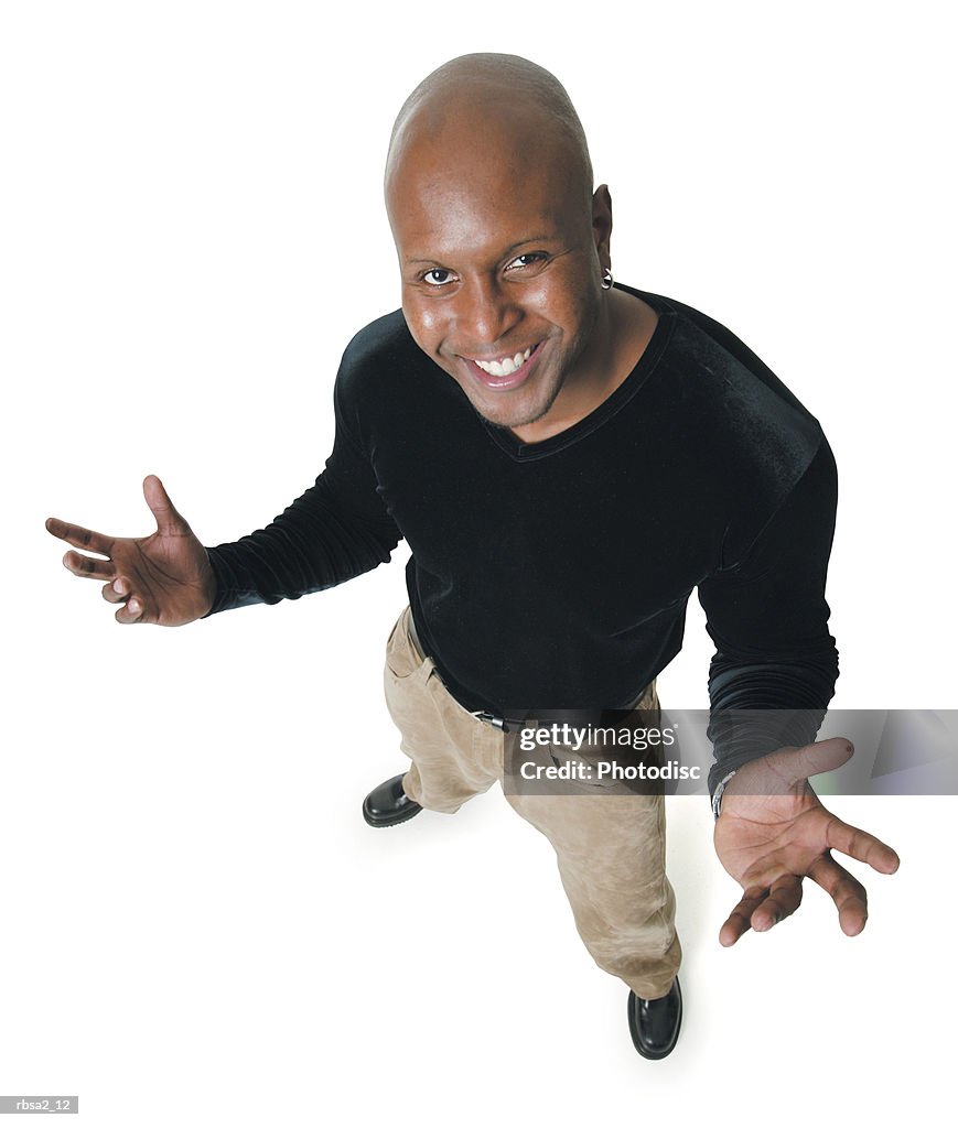 An african american man in tan pants and a black shirt puts his hands out and smiles up into the camera