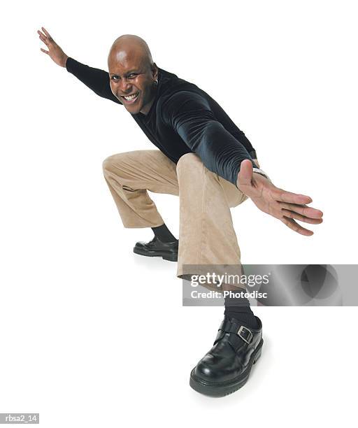 an african american man in tan pants and a black shirt bends down and spreads out his arms in a surfing pose - pants down bildbanksfoton och bilder