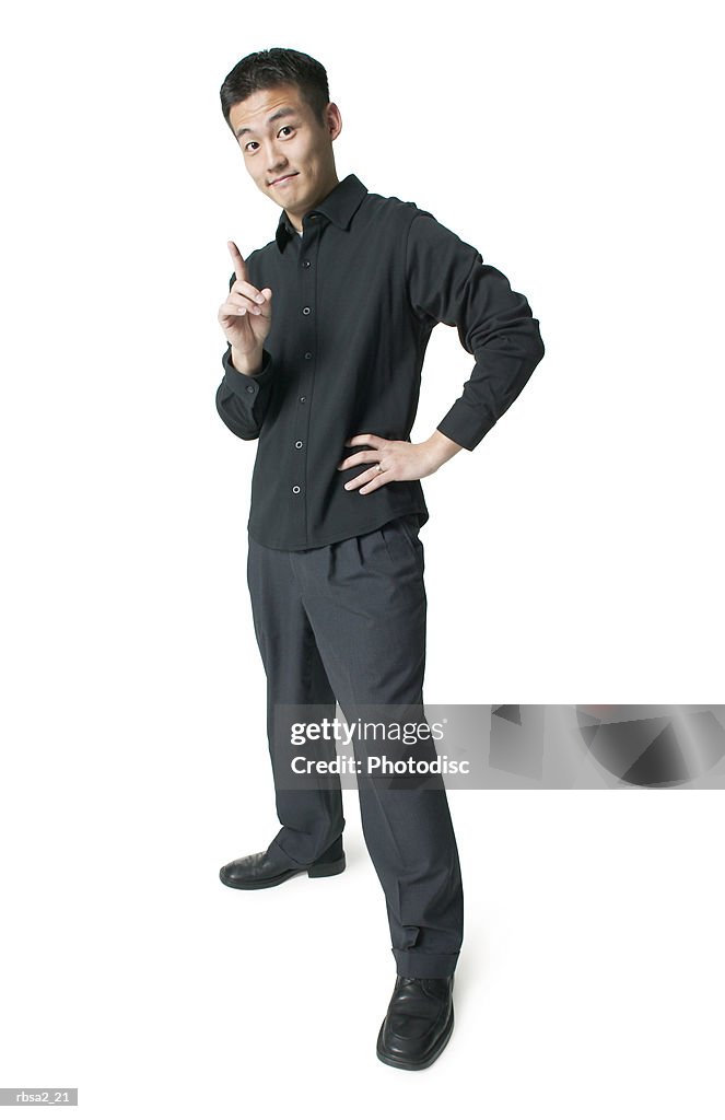 A young asian man dressed in black shakes his finger and smirks at the camera