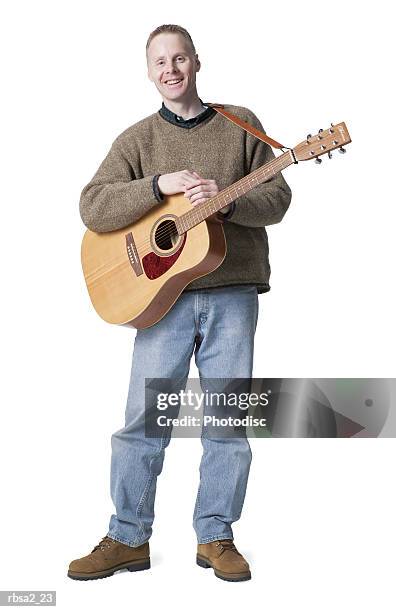 a caucasian man in jeans and a green sweater stand holds his guitar and smiles - guitar stand stock pictures, royalty-free photos & images