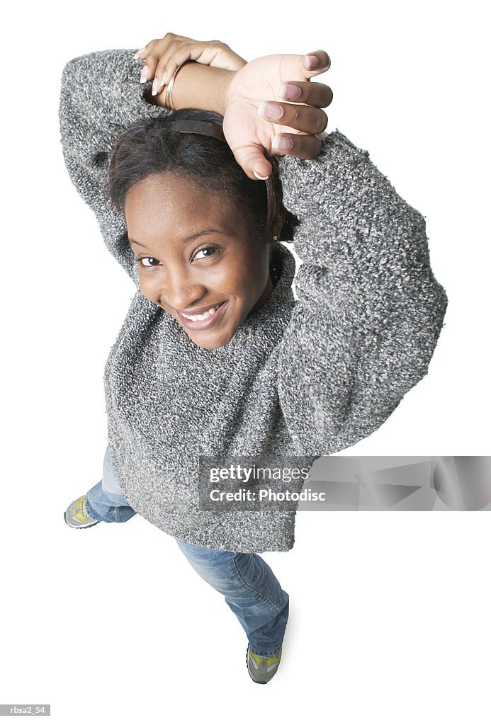 Young african american woman in jeans and grey sweater holds her arms over her head smiles to camera