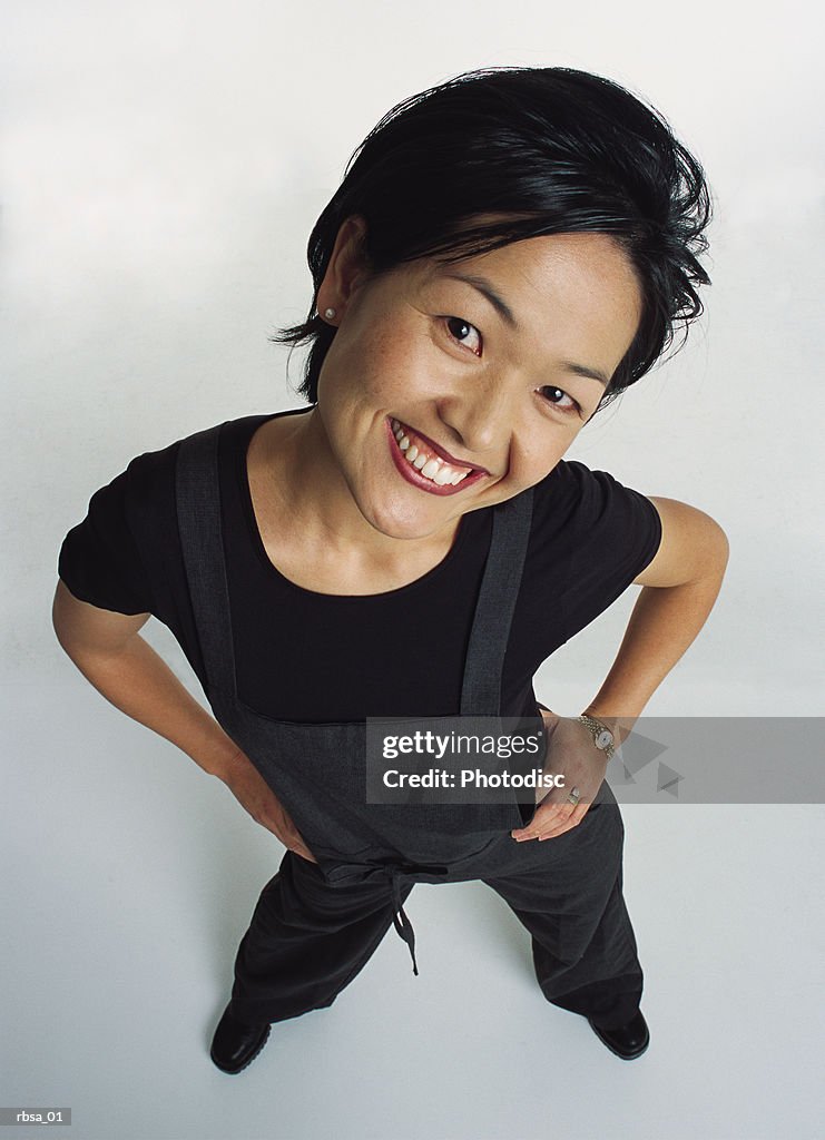 Young cute perky asian female adult wearing a dark jumper looks up at the camera with her head to one side while flirting and smiling amusingly