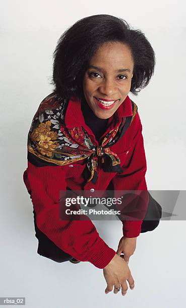 pretty middle aged african american adult female wearing a red blouse with a scarf over her shoulders kneels down while smiling up at the camera pleasantly - down blouse stockfoto's en -beelden