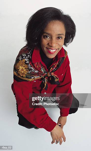 pretty middle aged african american adult female wearing a red blouse with a scarf over her shoulders kneels down while smiling up at the camera pleasantly - down blouse imagens e fotografias de stock