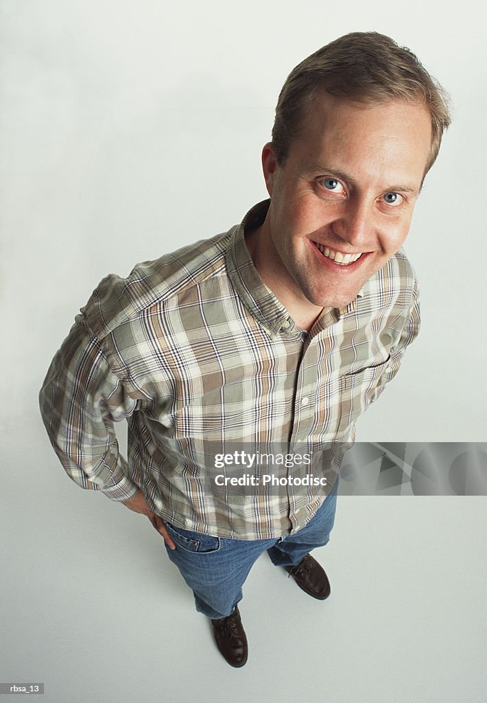 Clean-cut young adult male caucasian wearing a plaid shirt stands casually looking up at the camera and smiling