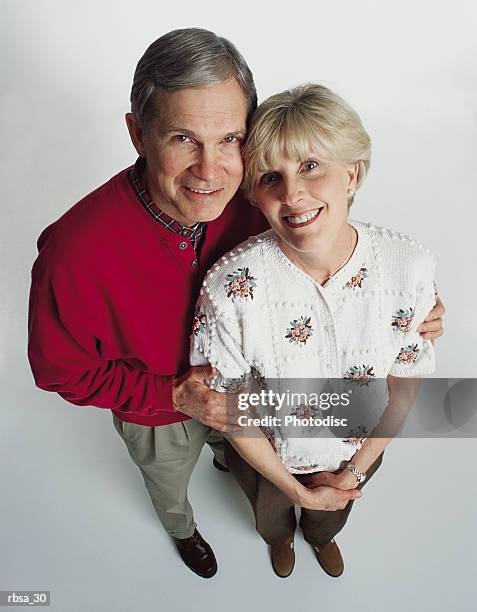 attractive old caucasian adults male red sweater stands with arms around female floral sweater smile - smile stockfoto's en -beelden