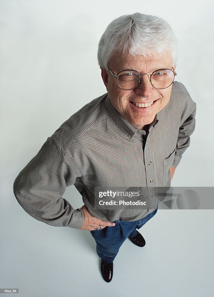 Handsome old caucasian adult male white hair glasses wears gray shirt jeans stands smiles to camera