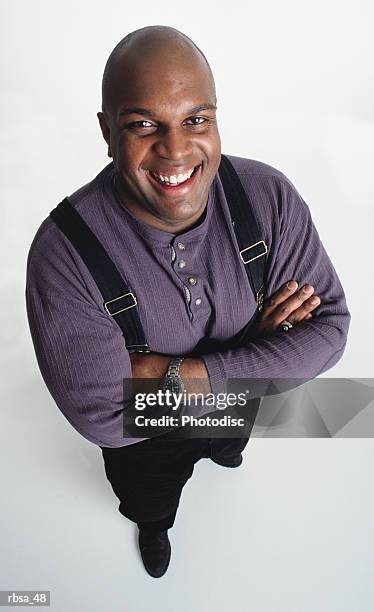 overweight middle aged african american adult male wearing a purple shirt and dark slacks with suspenders stands with arms folded looking up at the camera and smiling happily - black shirt folded stock pictures, royalty-free photos & images