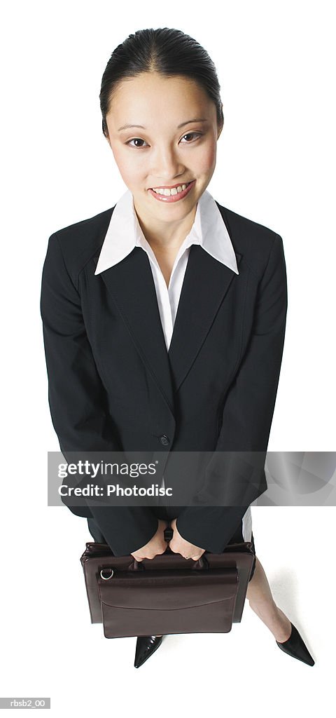 An attractive asian woman in a black business suit holds a briefcase and smiles up at the camera