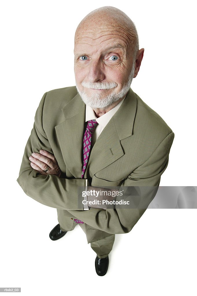 An elderly caucasian man with a beard in a green suit folds his arms and smirks up at the camera